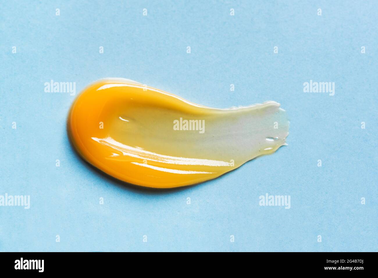 Échantillon de gel orange sur fond bleu, gros plan. Texture du produit cosmétique orange pour le soin des cheveux du visage. Banque D'Images