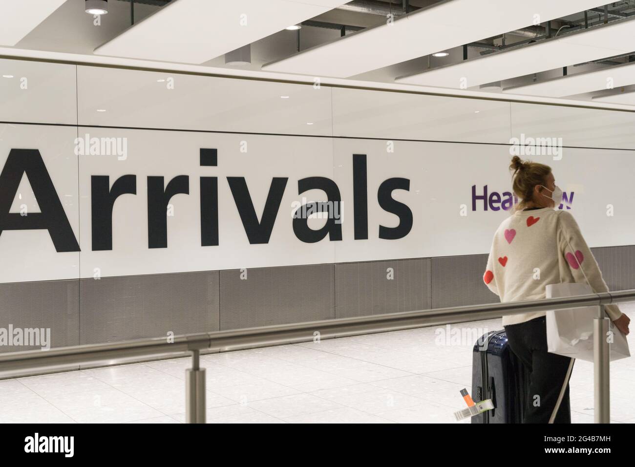 Femme en sweat-shirt blanc avec des imprimés en forme de coeur rouge est arrivée au hall des arrivées de Heathrow, couverture de visage, masque de visage, voyageur, Angleterre, ROYAUME-UNI Banque D'Images