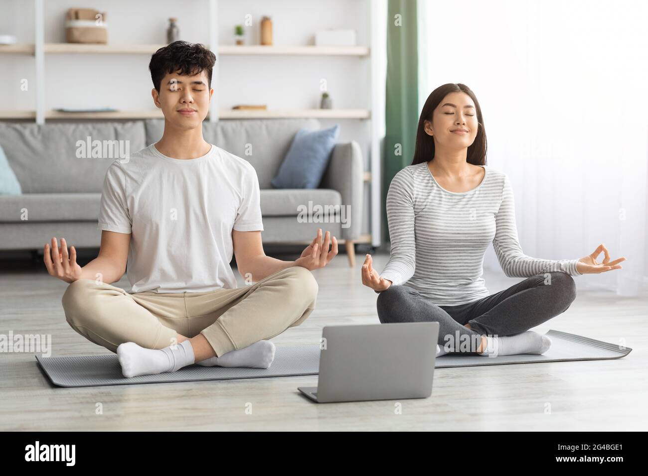 Paisible famille asiatique pratiquant la méditation à la maison, en utilisant un ordinateur portable Banque D'Images