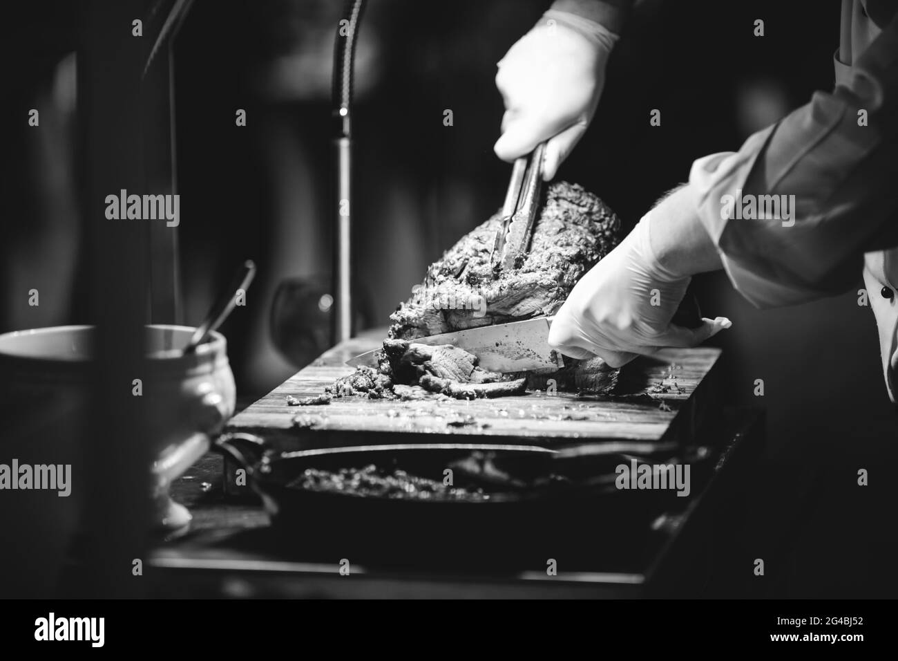 Détails de faible profondeur de champ (mise au point sélective) avec un chef cuisinier qui coupe des steaks de bœuf lors d'un événement exclusif. Banque D'Images