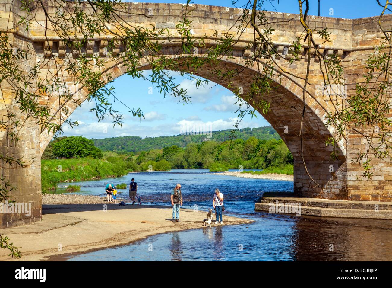 Les gens sur la plage de sable sous le pont voûté au-dessus de la rivière Tyne au village de Northumberland de Corbridge Angleterre construit en 1674 Banque D'Images