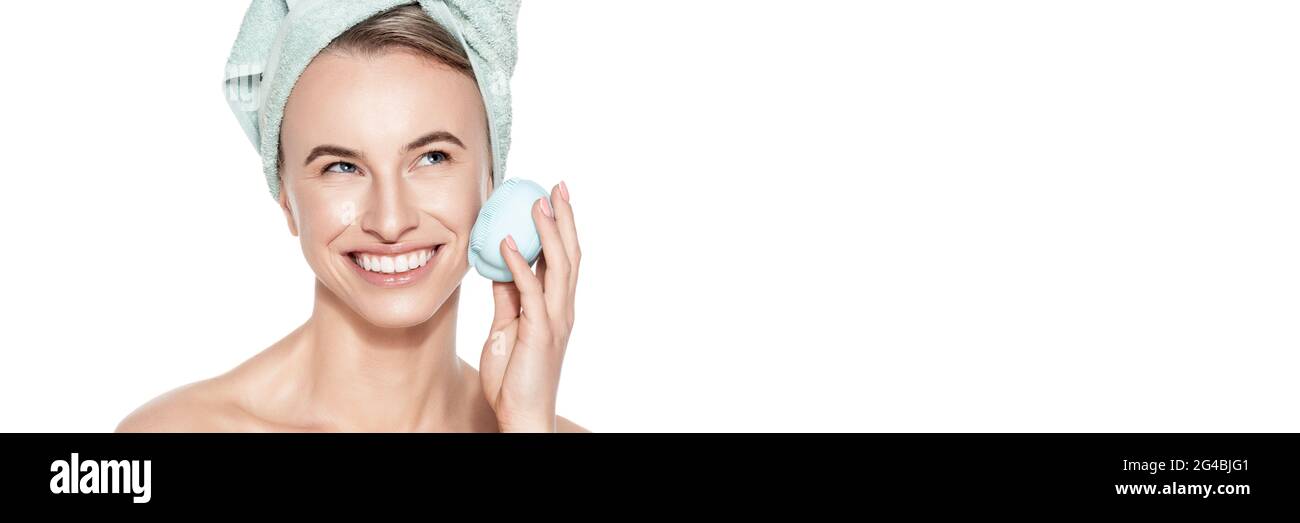 Jeune femme utilisant une brosse nettoyante en silicone pour le visage. Portrait de concept de beauté et de soin de la peau sur blanc. Exfoliation, massage du visage, démaquillage bann Banque D'Images