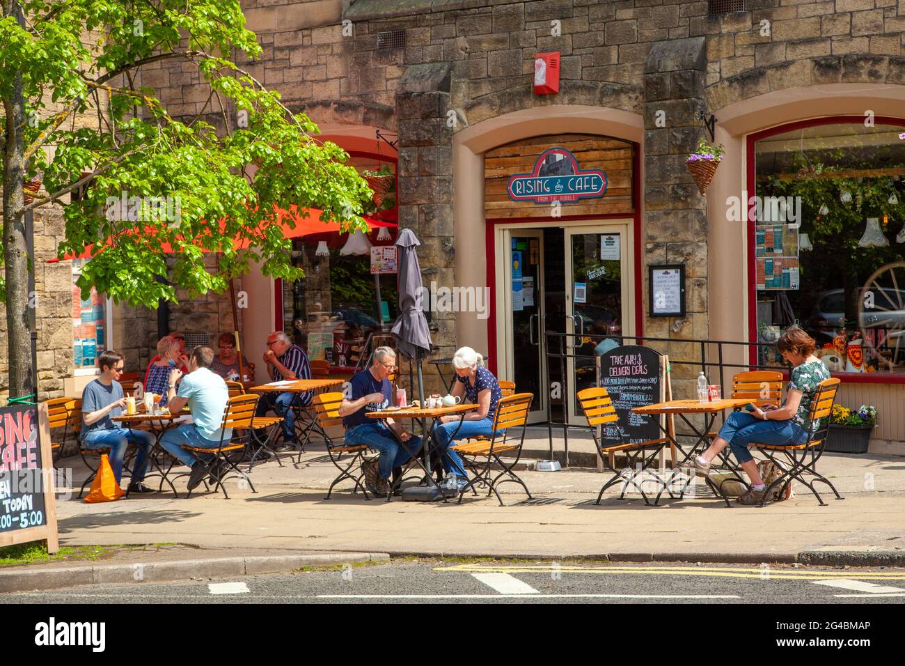 Les gens assis dehors en profitant du soleil manger et boire dans un café sur le trottoir dans la ville marchande de Northumberland, Hexham Angleterre Banque D'Images