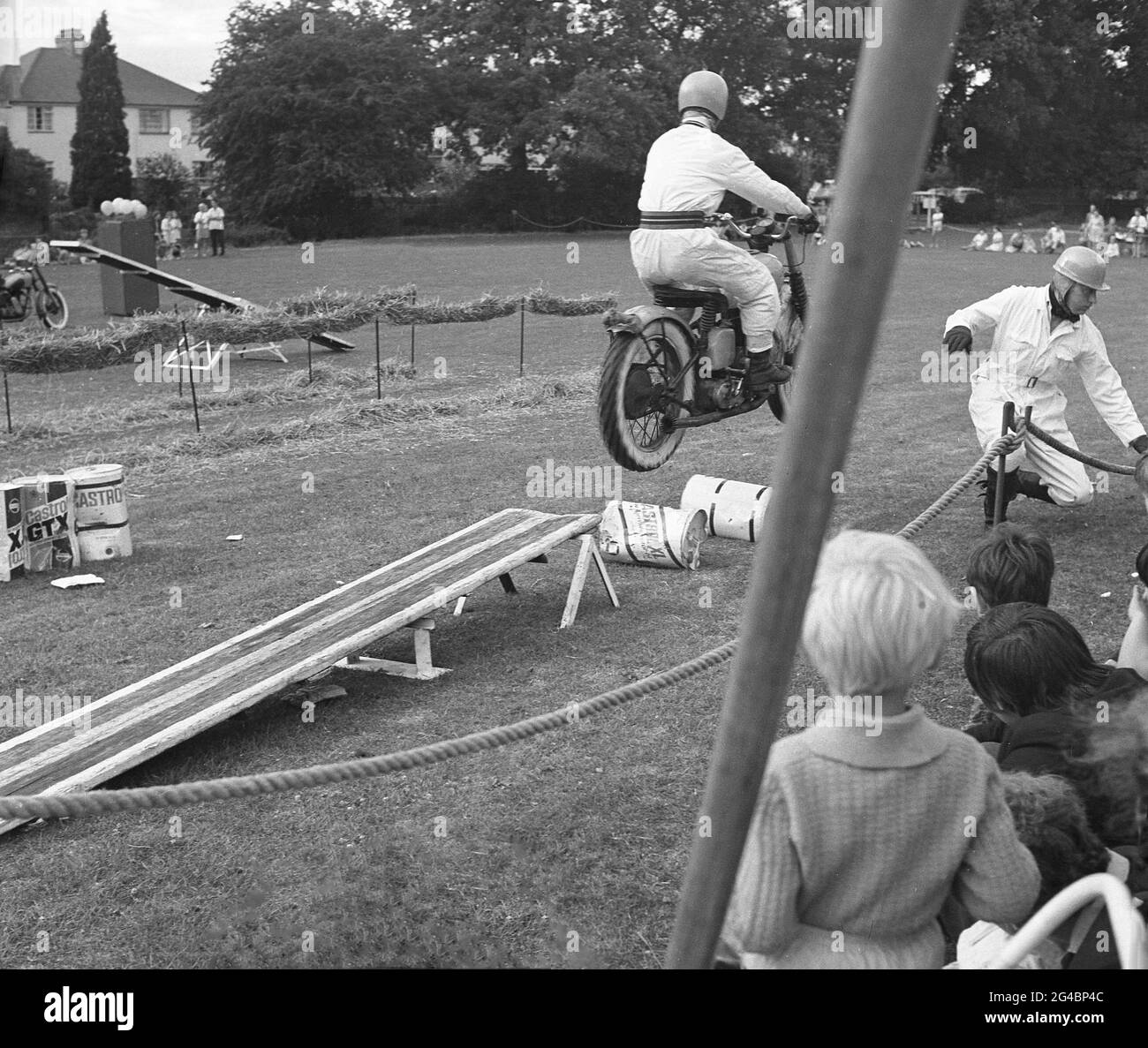 années 1960, historique, à l'extérieur d'un champ, un membre d'une équipe d'exposition de moto effectuant une cascade de sauter au-dessus des bidons d'huile sur son moto. Les expositions acrobatiques de motos à l'extérieur des carnavals et des événements spéciaux ont été populaires à cette époque, avec les signaux royaux, les 'casques blanc', une équipe d'exposition de l'armée britannique, le plus connu. Ils avaient réalisé le premier affichage de cascades enregistré en 1928 alors que les pilotes de l'armée, qui étaient un élément clé des communications de l'armée à ce moment-là, devaient être des motocyclistes hautement qualifiés. Banque D'Images