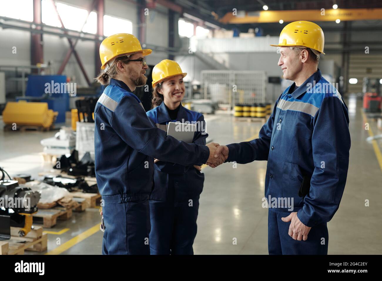 Content mature Factory Executive dans hardhat félicitant les travailleurs avec la mise en œuvre de plan de travail et de serrer la main de l'un d'entre eux dans l'entrepôt Banque D'Images