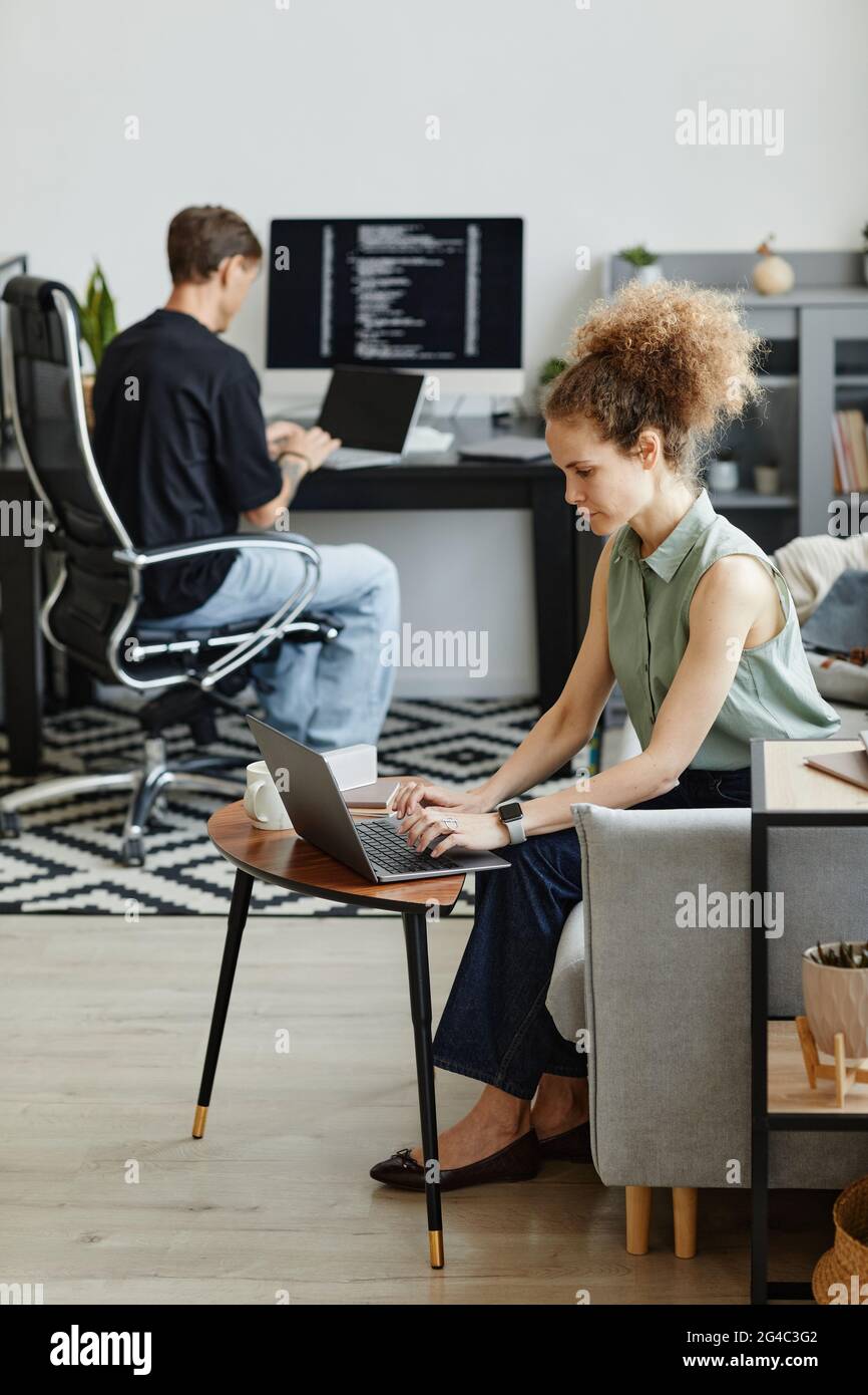 Femme d'affaires mûre assise sur un canapé et travaillant sur un ordinateur portable avec son collègue utilisant un ordinateur portable aussi en arrière-plan Banque D'Images