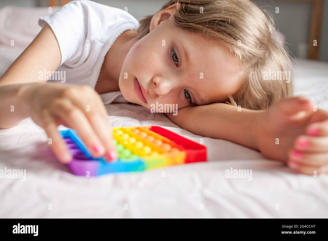 Petite fille joue avec le jouet sensoriel branché pop. La jeune fille appuie sur des bulles de silicone souple arc-en-ciel colorées. Soulagement du stress et de l'anxiété. Banque D'Images