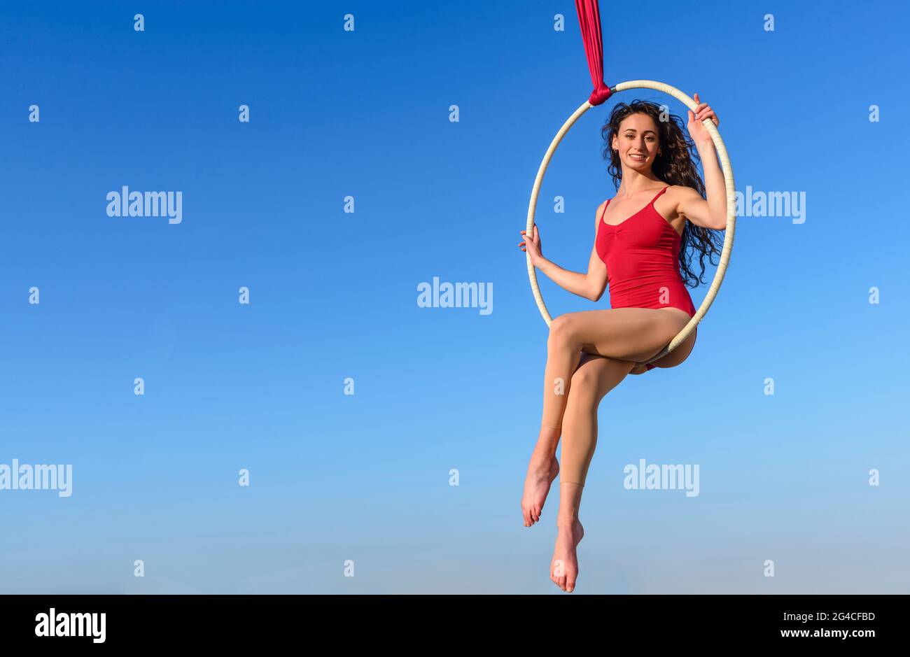 acrobat athlétique, jeune gracieuse gymnaste portrait sur anneau aérien à l'extérieur sur fond de ciel. flexible femme en costume rouge interprète la danse d'artiste de cirque Banque D'Images