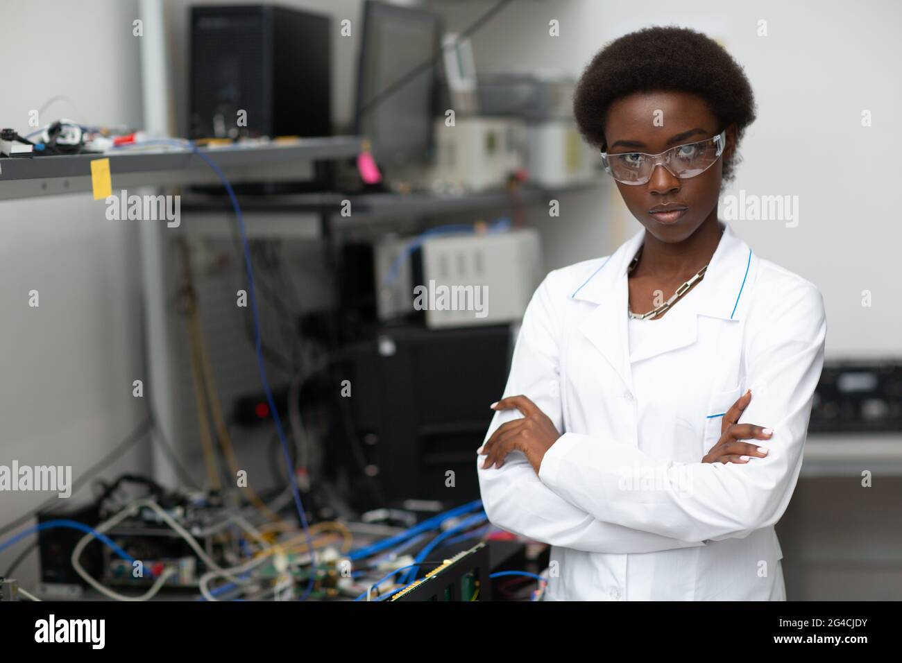 Scientifique afro-américaine femme avec des lunettes de protection debout et regardant la caméra en laboratoire avec des instruments électroniques de technologie. Banque D'Images