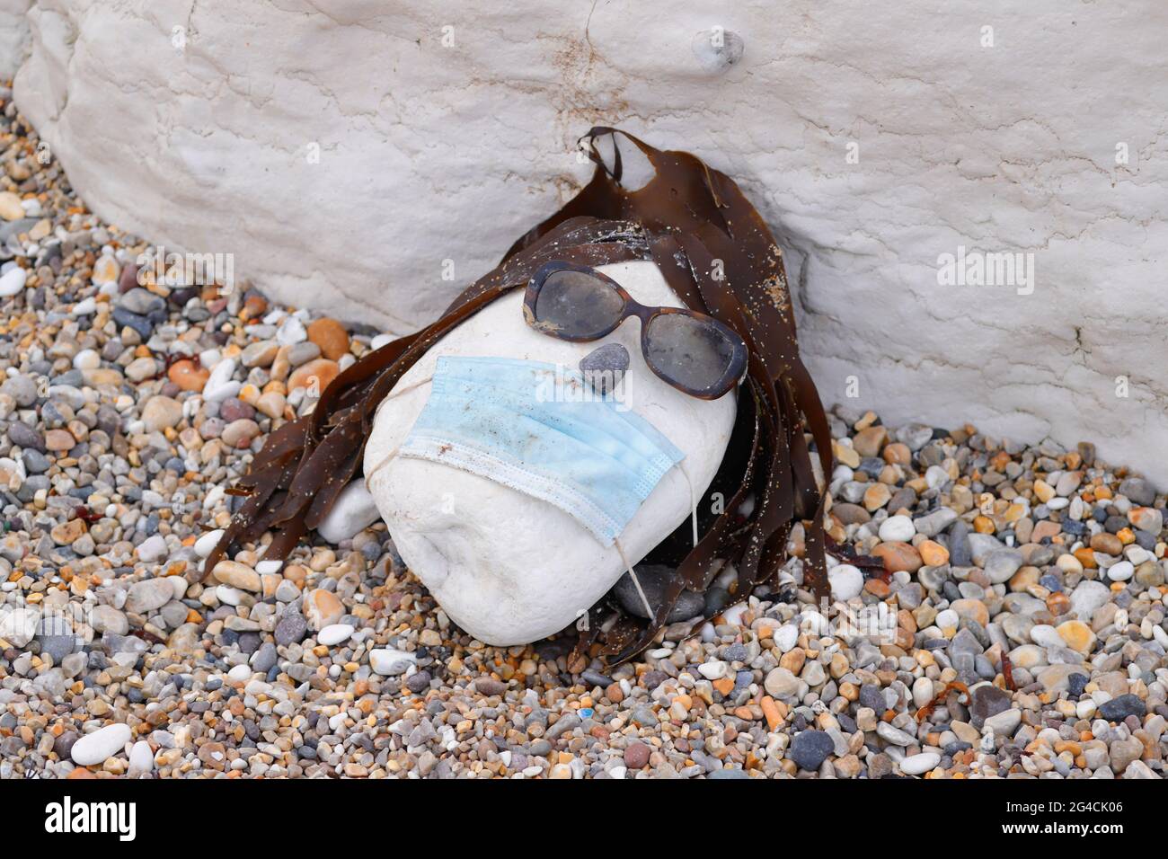 Un visage fait d'un galet, de lunettes de soleil, d'algues et d'un masque Covid, trouvé sur une plage à Thornwick Bay, East Yorkshire, Royaume-Uni Banque D'Images