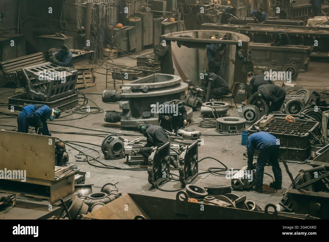 Grand atelier avec des travailleurs d'usine métallurgique travaillant avec des pièces en fonte, traitement post-moulage dans une fonderie d'aciérie. Banque D'Images