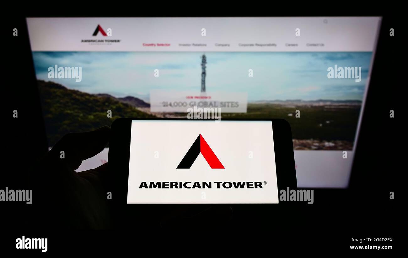 Personne tenant un téléphone portable avec le logo de la société d'infrastructure américaine American Tower Corp. À l'écran devant la page Web d'affaires. Mise au point sur l'affichage du téléphone. Banque D'Images