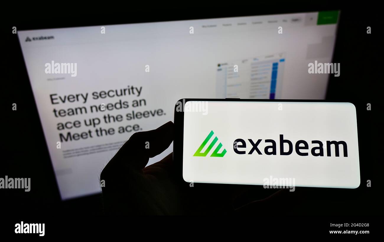 Personne portant un smartphone portant le logo de la société américaine de cybersécurité Exabeam Inc. À l'écran devant le site Web. Mise au point sur l'affichage du téléphone. Banque D'Images