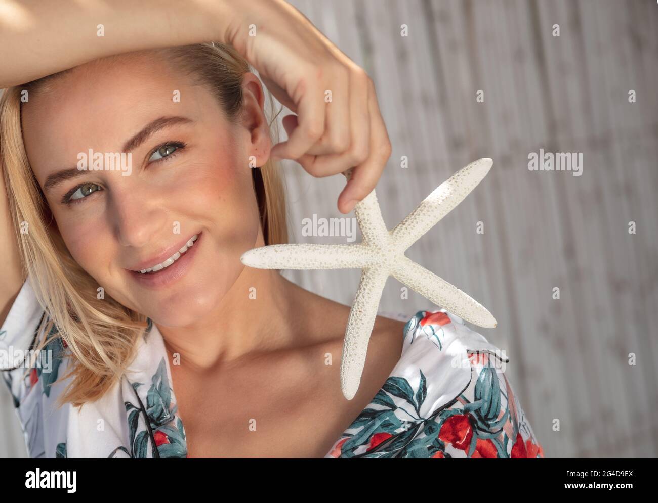 Portrait authentique d'une jolie femme avec Sea Star à la main posant à l'extérieur. Profitez de la lumière du soleil sur la plage. Vacances d'été sans soucis. Banque D'Images
