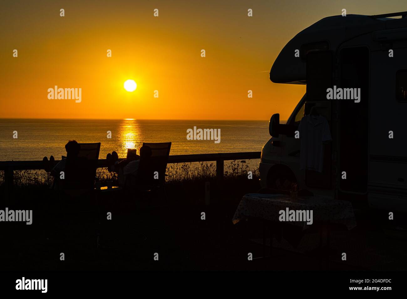 Magnifique coucher de soleil de l'heure d'or avec un couple se relaxant à côté d'un minibus de camping et profiter du coucher de soleil d'été à Cornwall Angleterre Royaume-Uni Banque D'Images