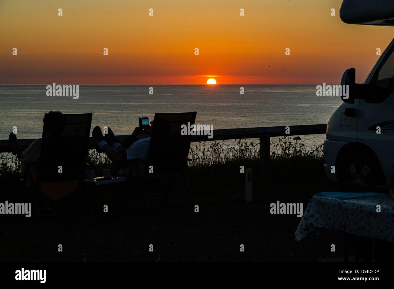 Magnifique coucher de soleil de l'heure d'or avec un couple se relaxant à côté d'un minibus de camping et profiter du coucher de soleil d'été à Cornwall Angleterre Royaume-Uni Banque D'Images Magnifique coucher de soleil de l'heure d'or avec un couple se relaxant à côté d'un minibus de camping et profiter du coucher de soleil d'été à Cornwall Angleterre Royaume-Uni Banque D'Images