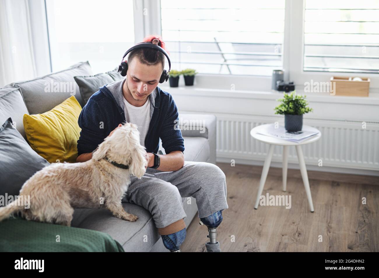 Portrait d'un jeune homme handicapé jouant avec un chien à l'intérieur à la maison, concept prothétique de jambe. Banque D'Images