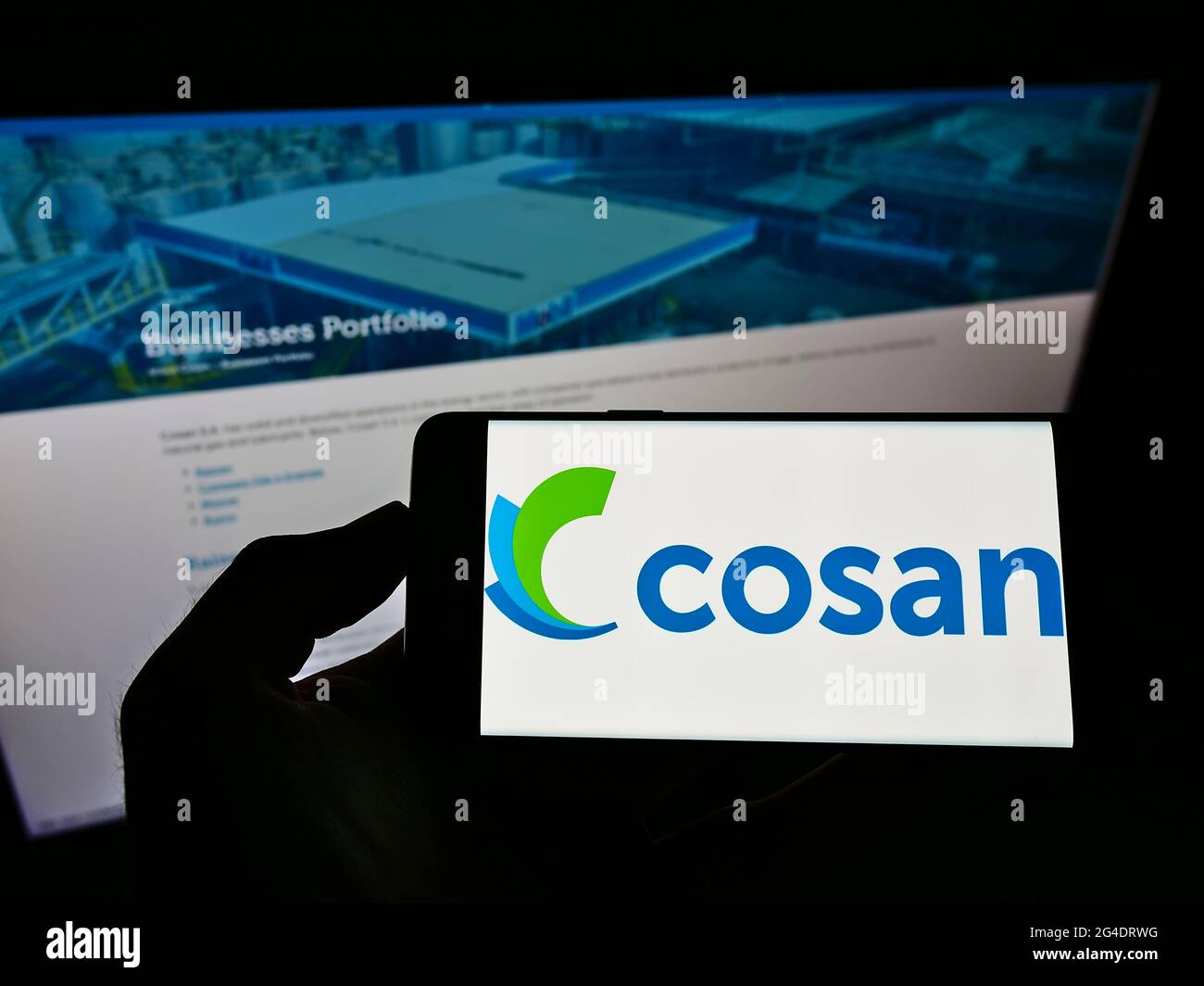 Personne tenant un téléphone mobile avec le logo du conglomérat brésilien Cosan S.A. à l'écran en face de la page Web d'affaires. Mise au point sur l'affichage du téléphone. Banque D'Images