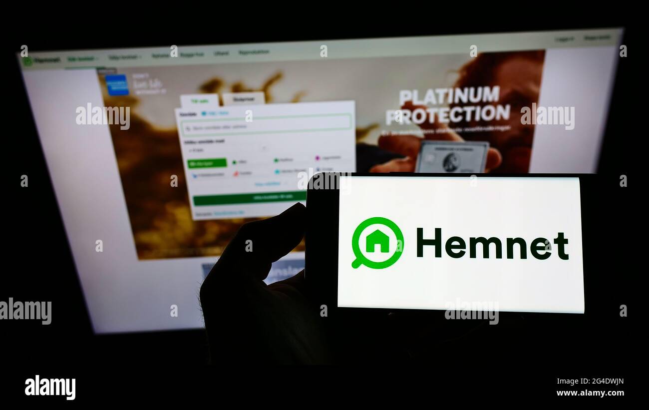 Personne tenant un smartphone avec le logo de la société suédoise de plate-forme immobilière Hemnet AB à l'écran devant le site Web. Mise au point sur l'affichage du téléphone. Banque D'Images