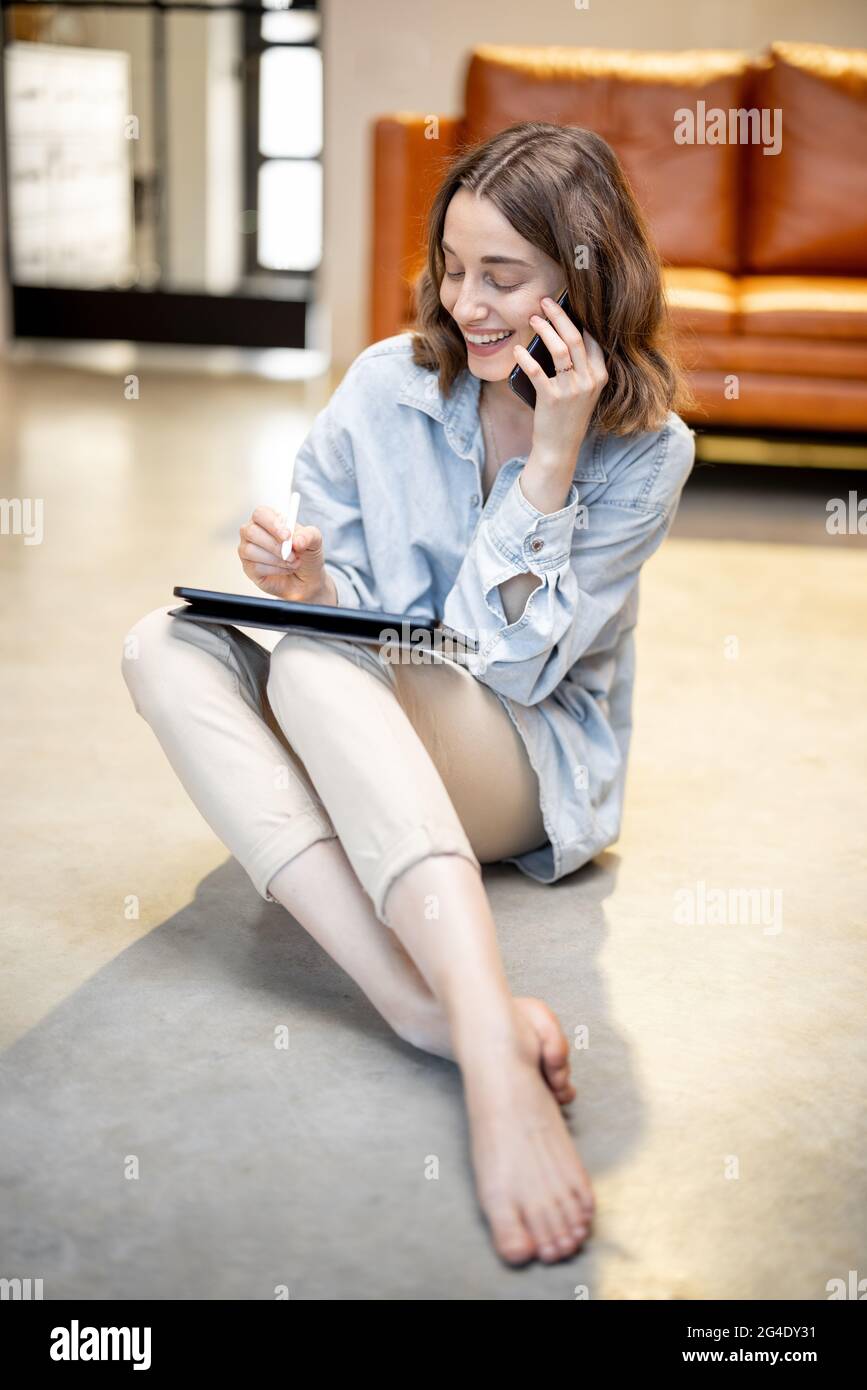 Femme travaille sur une tablette numérique tout en étant assise sur le sol Banque D'Images