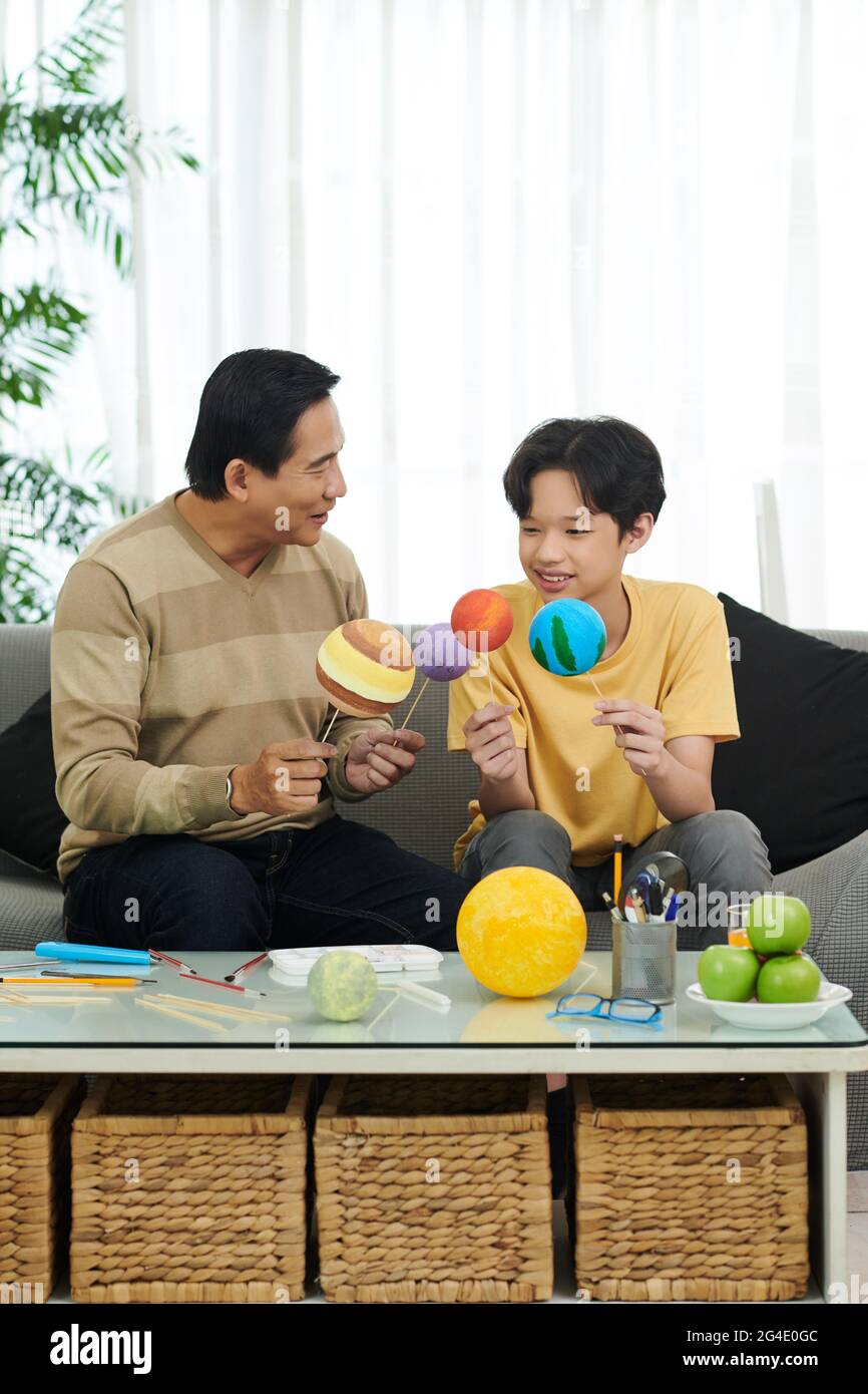 Père et fils excités mettant des boules peintes sur bâton de bois pour le laisser sécher lors de la finition du modèle de système solaire pour l'école Banque D'Images