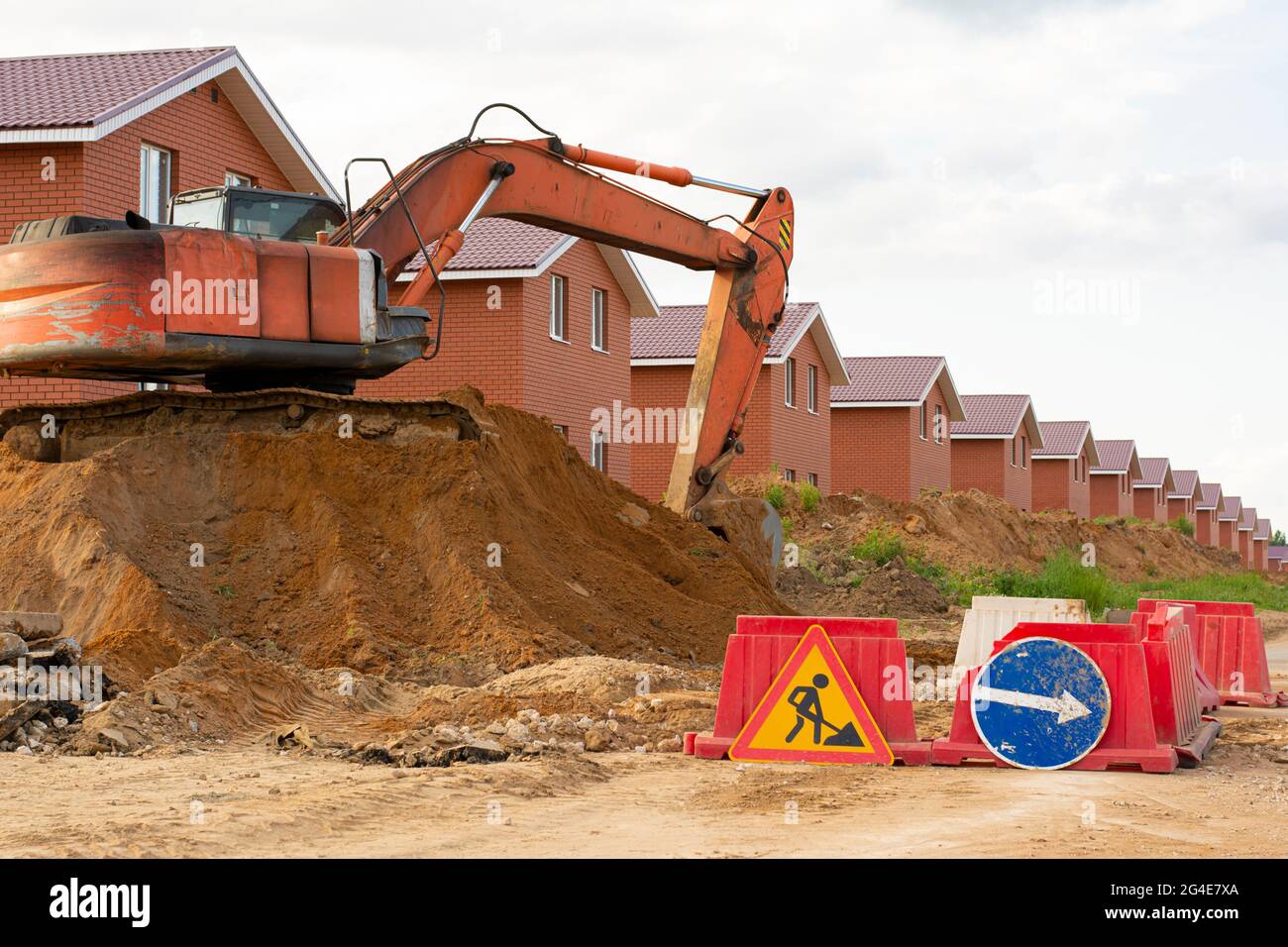 Le tracteur d'équipement de construction avec godet creuse le sol près de la route. Un bulldozer à chenilles métalliques. Construction de maisons de deux étages. Banque D'Images