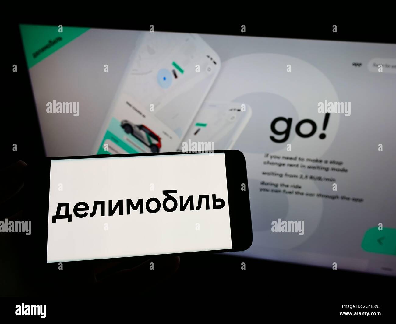 Personne tenant le téléphone portable avec le logo de la compagnie russe de partage de voitures Delimobil sur l'écran en face de la page web d'affaires. Mise au point sur l'affichage du téléphone. Banque D'Images