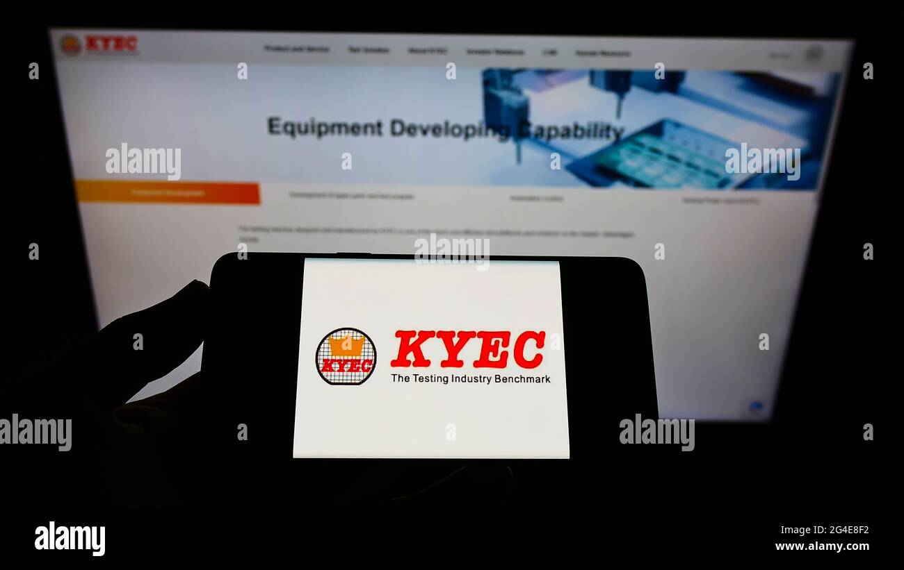 Personne tenant un téléphone portable avec le logo de la société taïwanaise King Yuan Electronics Corp. (KYEC) à l'écran en face de la page Web. Mise au point sur l'affichage du téléphone. Banque D'Images