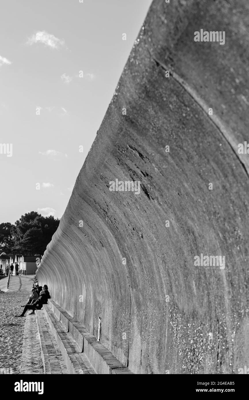 Personnes assises sur UN mur de mer en béton incurvé en noir et blanc à Avon Beach Christchurch Royaume-Uni Banque D'Images