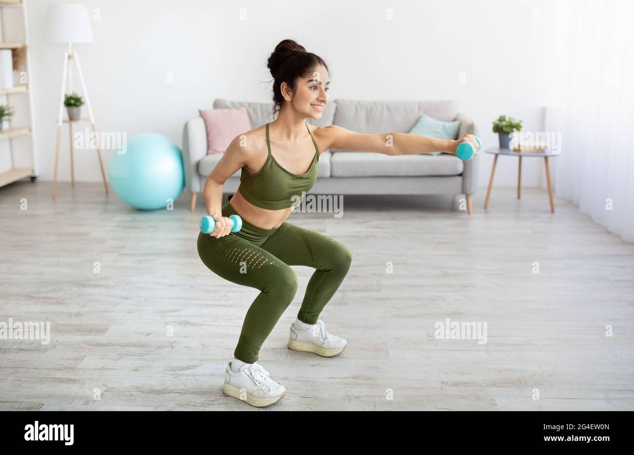 Bonne jeune femme indienne faisant des squats avec des haltères à la maison, pleine longueur Banque D'Images