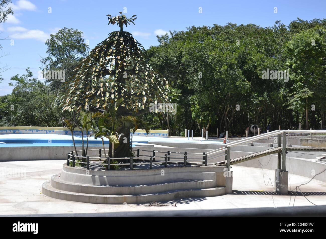 Sculpture en fer qui ressemble à un arbre dans un hôtel d'écotourisme avec vue panoramique avec une piscine et des arbres dans le fond contre un ciel bleu avec des nuages Banque D'Images