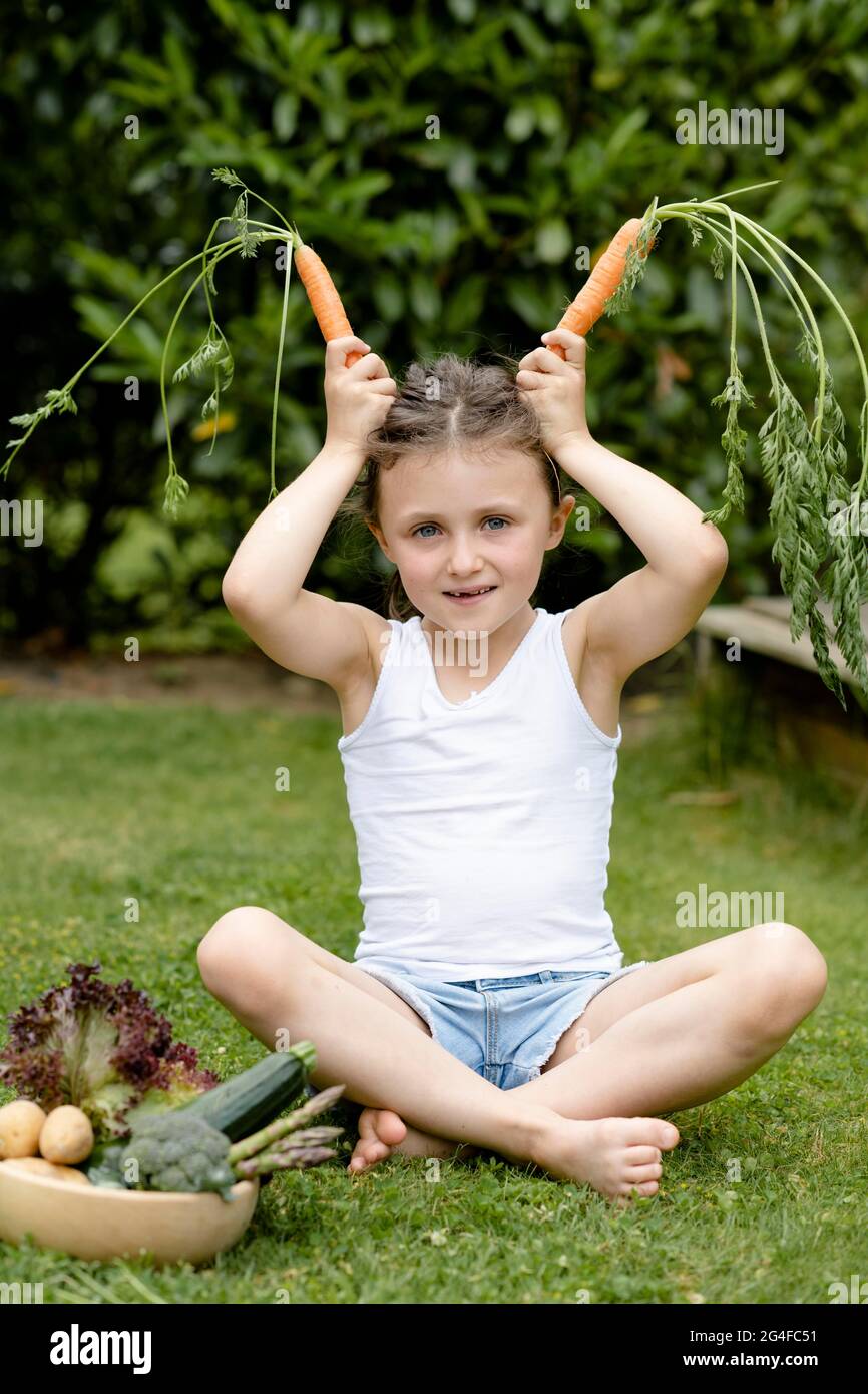 Elle est assise dans la prairie et montre des oreilles de lapin avec des carottes Banque D'Images