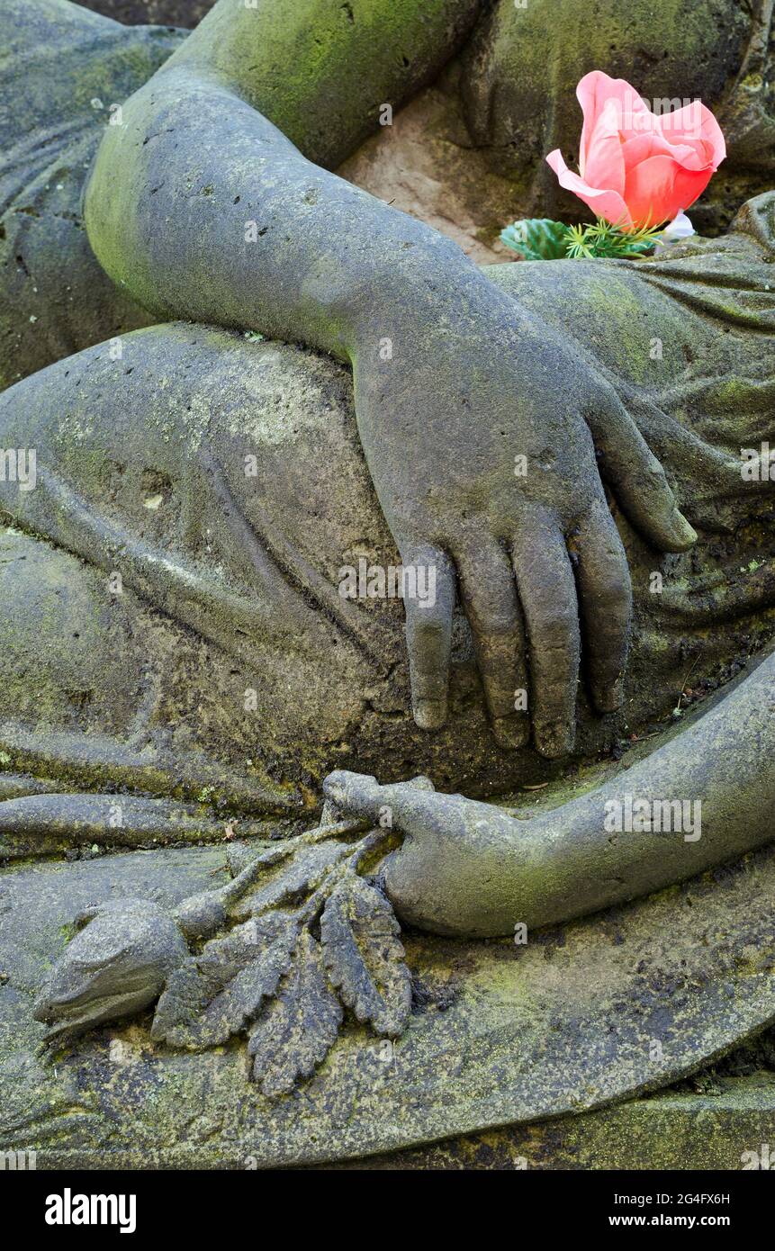 Statue en deuil de la mère et de l'enfant mourant, gros plan avec les mains et la fleur rose Banque D'Images