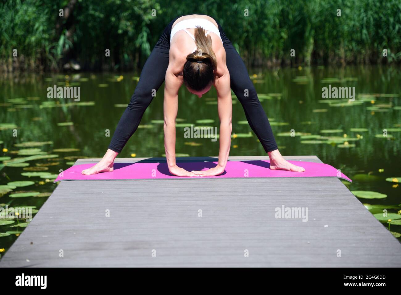 Femme dans ses années 30 pratiquant le yoga et la méditation. Posez la femme sur une plate-forme en bois à l'étang, entourée d'arbres et d'eau. Banque D'Images