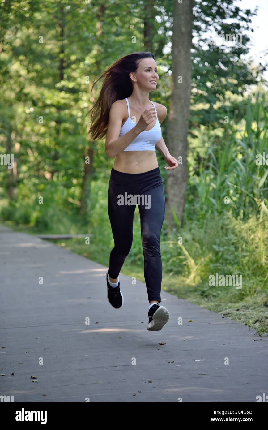 Faire du jogging de 30 ans à une femme dans le parc. Jeune femme avec pantalon noir et haut blanc dans le parc. Banque D'Images