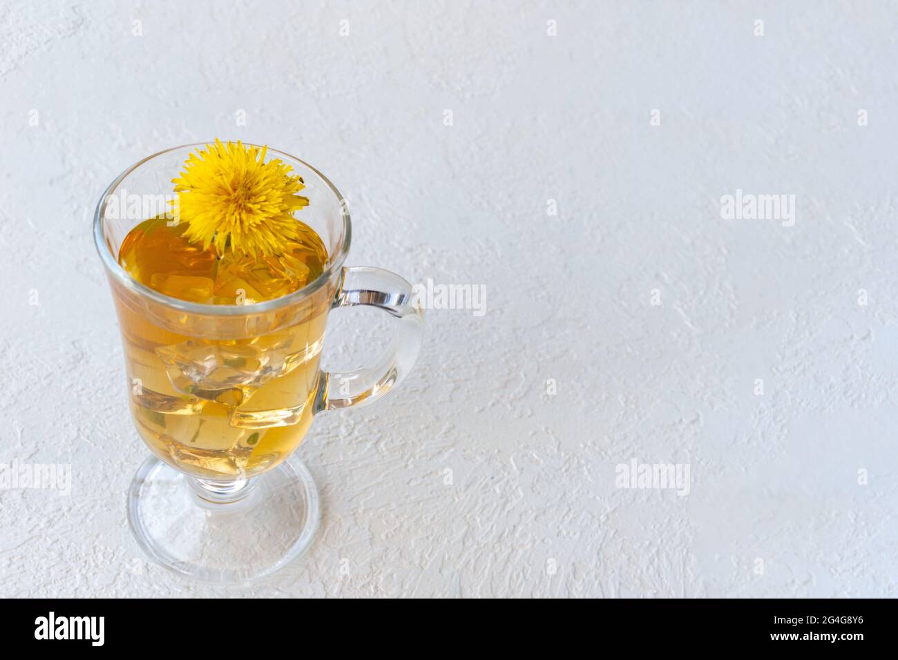 Thé de pissenlit à base de plantes saines dans une tasse de verre et fleur de pissenlit jaune à l'intérieur sur fond blanc, espace de copie, gros plan. Boisson rafraîchissante en été. H Banque D'Images