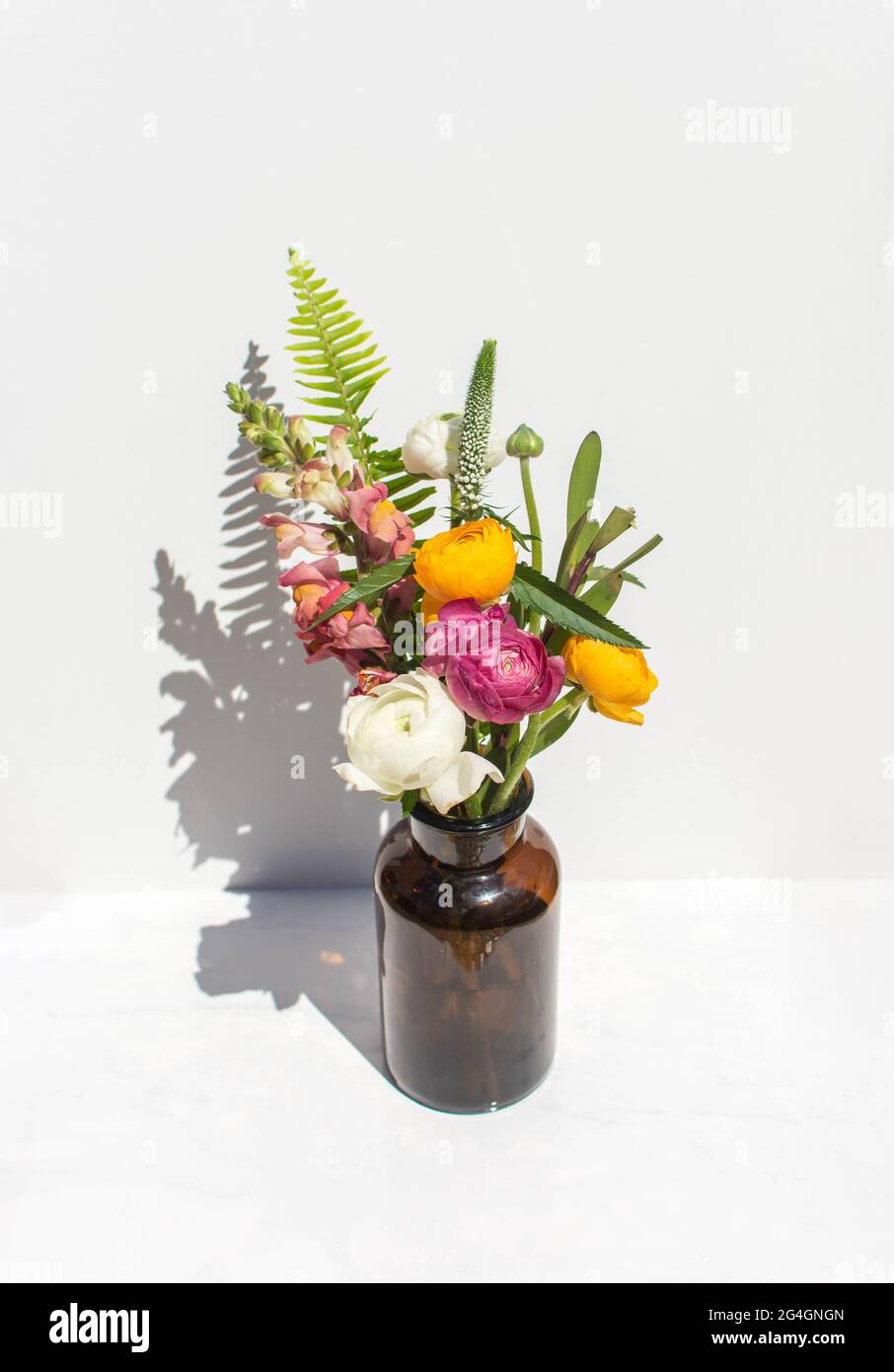 Bouquet d'été lumineux dans un vase ambre sur fond de marbre blanc. La vie éditoriale est encore sous un soleil éclatant. Banque D'Images