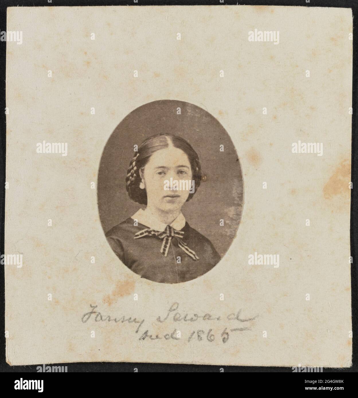 Imprimé en albumine de Fanny Seward montré en portrait de buste. L'impression est découpée dans un ovale et collée sur un support papier. Seward fait face à la caméra avec ses cheveux séparés au centre et rassemblés dans une écharpe derrière sa tête. Elle porte un corsage de couleur foncée, blanc standard col, Et un ruban de couleur claire et sombre est attaché dans un arc à l'avant de son cou.;manuscrit en graphite sur le fond au centre de la monture est le texte "Fanny Seward / Darden 1865".;la photographie est contenue dans l'album 2017.30. La page de l'album est dotée d'une bordure dorée à trois lignes qui encadre l'impression. Banque D'Images