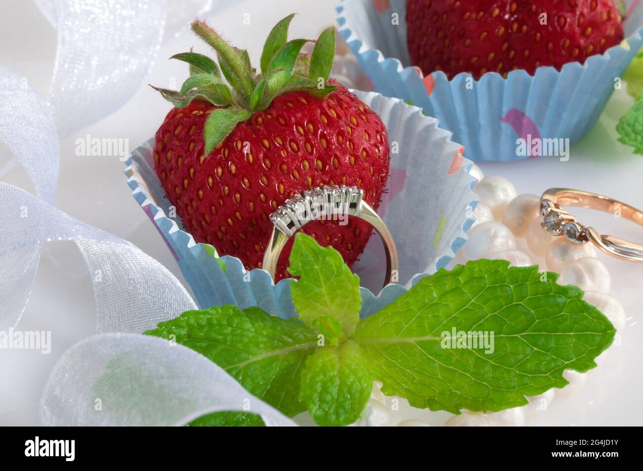 Ensemble de bijoux avec des diamants dans un moule de cupcake en papier avec une fraise juteuse à l'intérieur. Banque D'Images