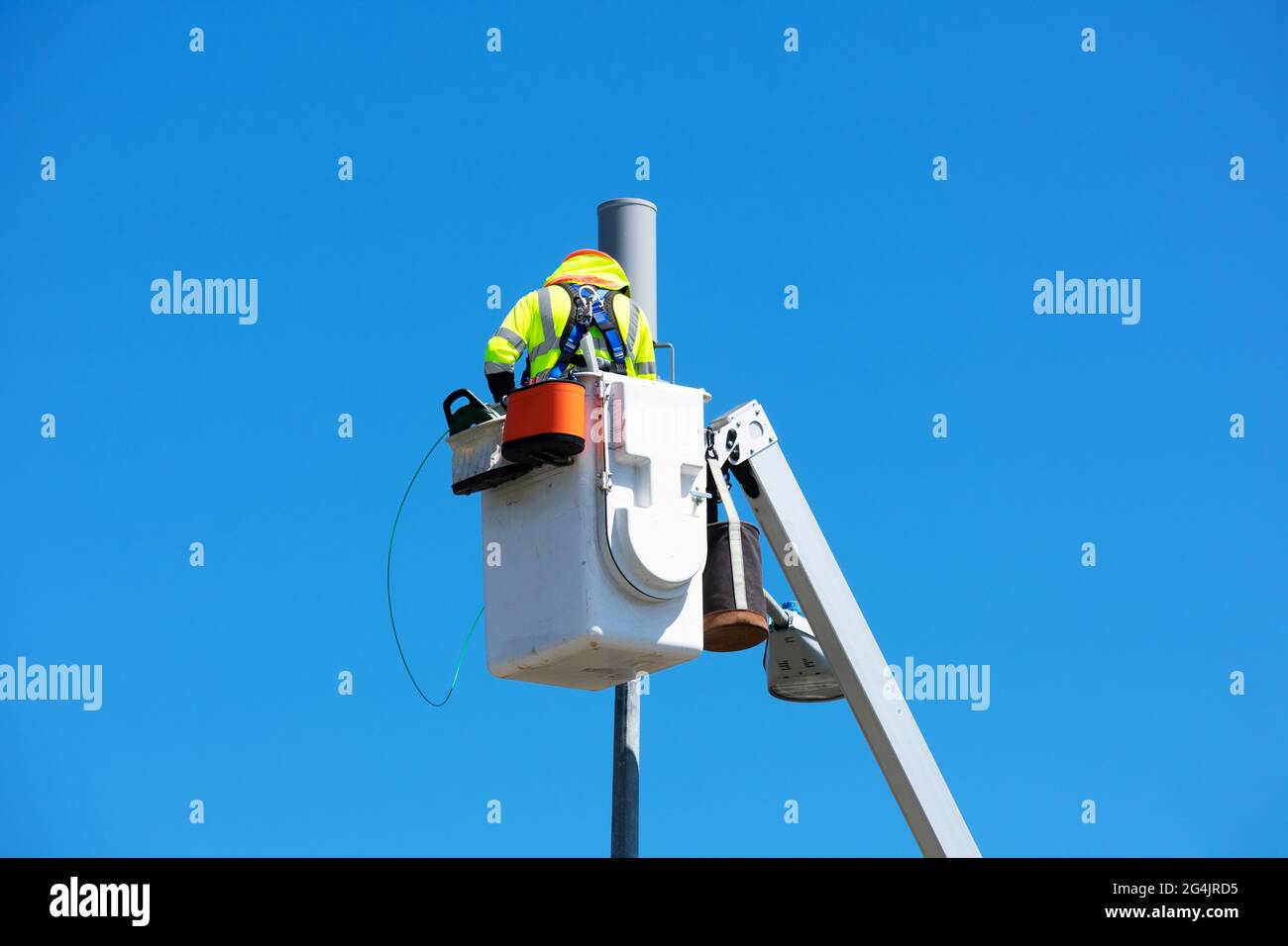 Le technicien travaille à l'installation ou à la réparation d'une petite antenne cellulaire sur un montant de lampe depuis la plate-forme du relevage de la flèche télescopique. Ciel bleu. Banque D'Images