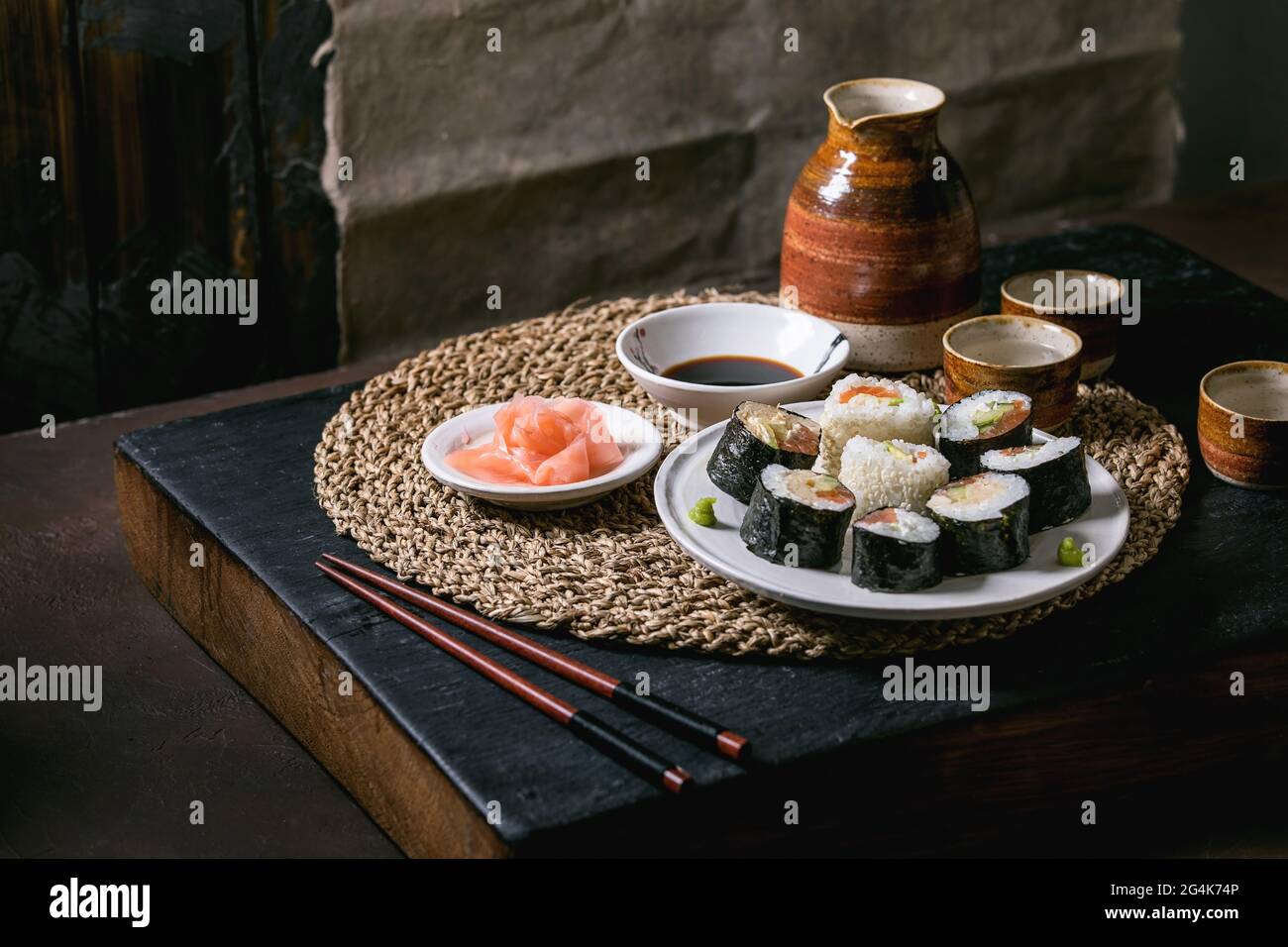 Petits pains à sushis faits maison au saumon, omelette japonaise, avacado, gingembre et sauce soja avec baguettes sur serviette en paille. Table en bois de balck. Céramique sa Banque D'Images