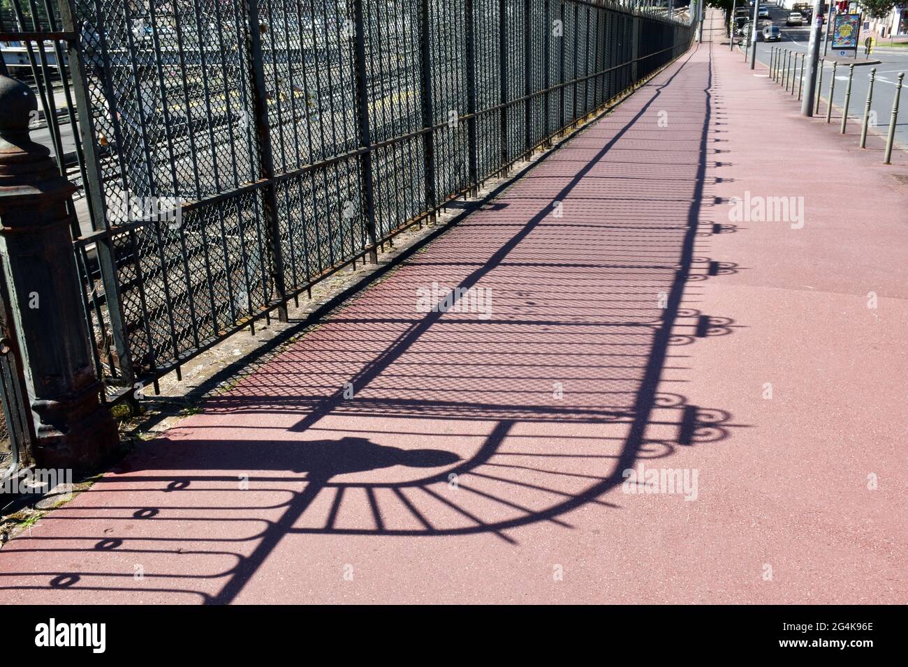 Clôture en fonte et en fer forgé à côté des voies ferrées menant à la gare de Limoges Bénédictine, jetant une ombre intéressante sur un pavé d'asphalte rouge immaculé Banque D'Images