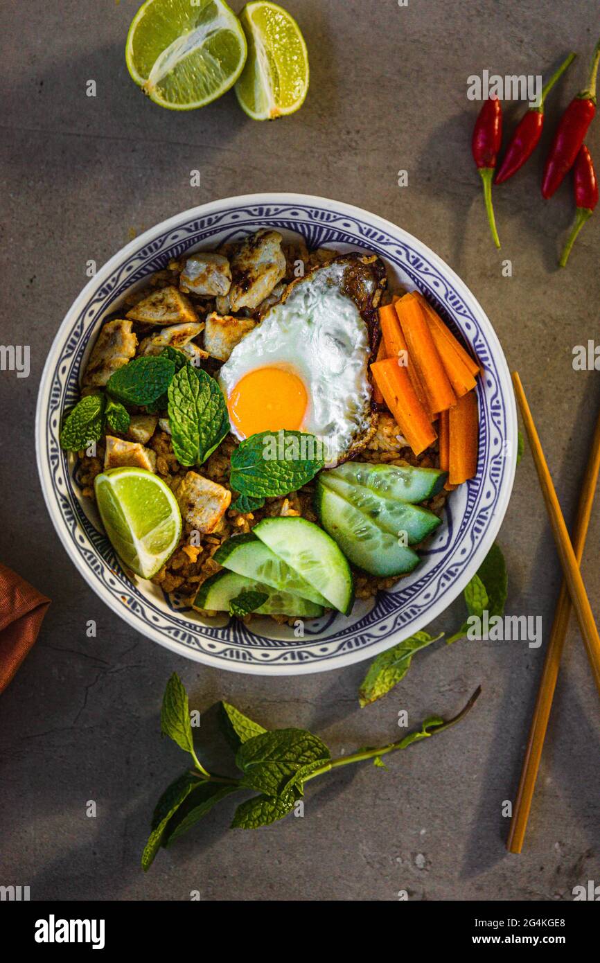 Riz indonésien Nasi goreng frit avec un œuf frit, du concombre frais, de la carotte, de la menthe, du citron vert et du Chili Banque D'Images