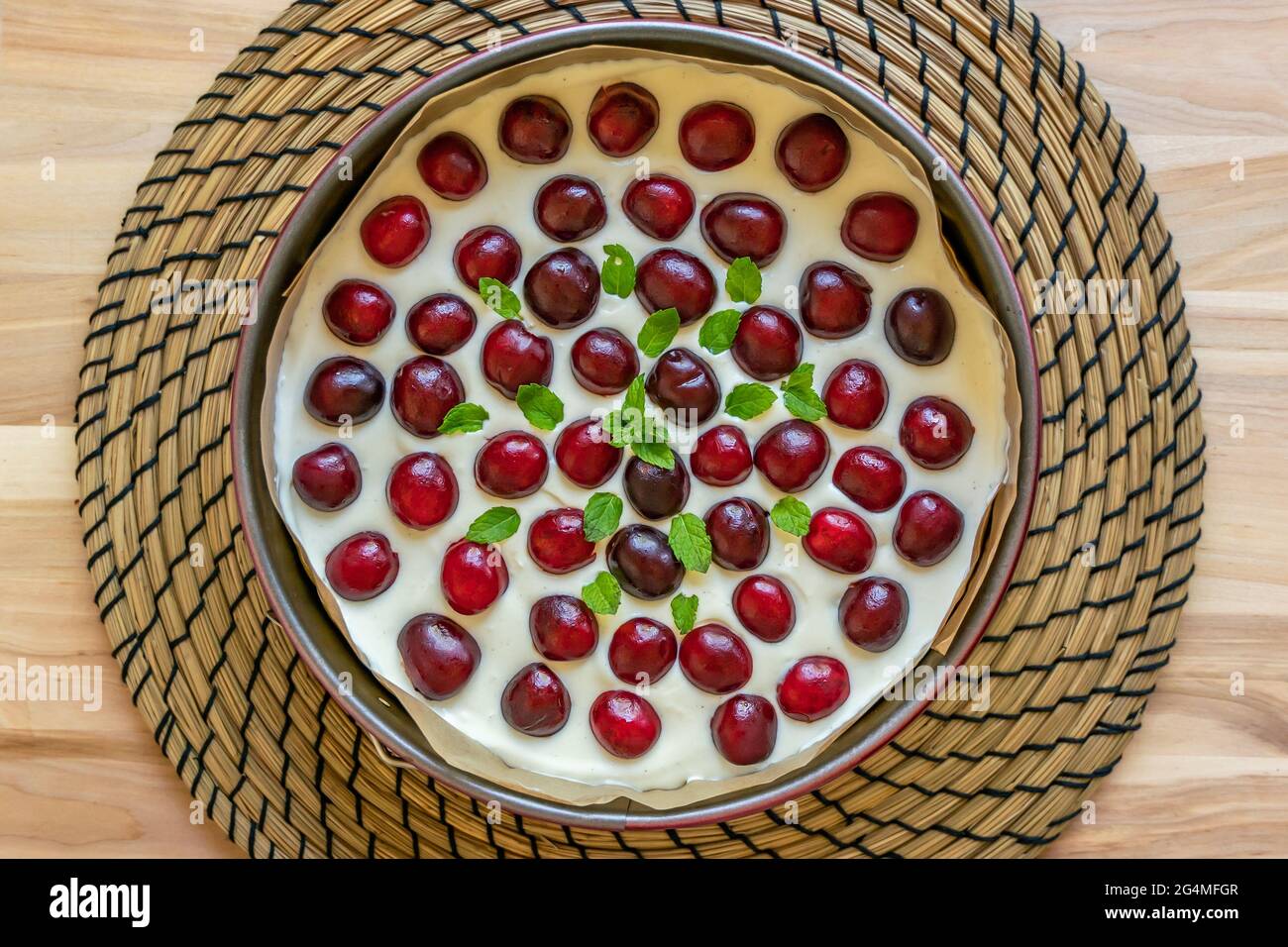 Gros plan du cheesecake maison est recouvert de cerises fraîches et d'une branche de menthe dans un moule à gâteau rond sur une table en bois Banque D'Images
