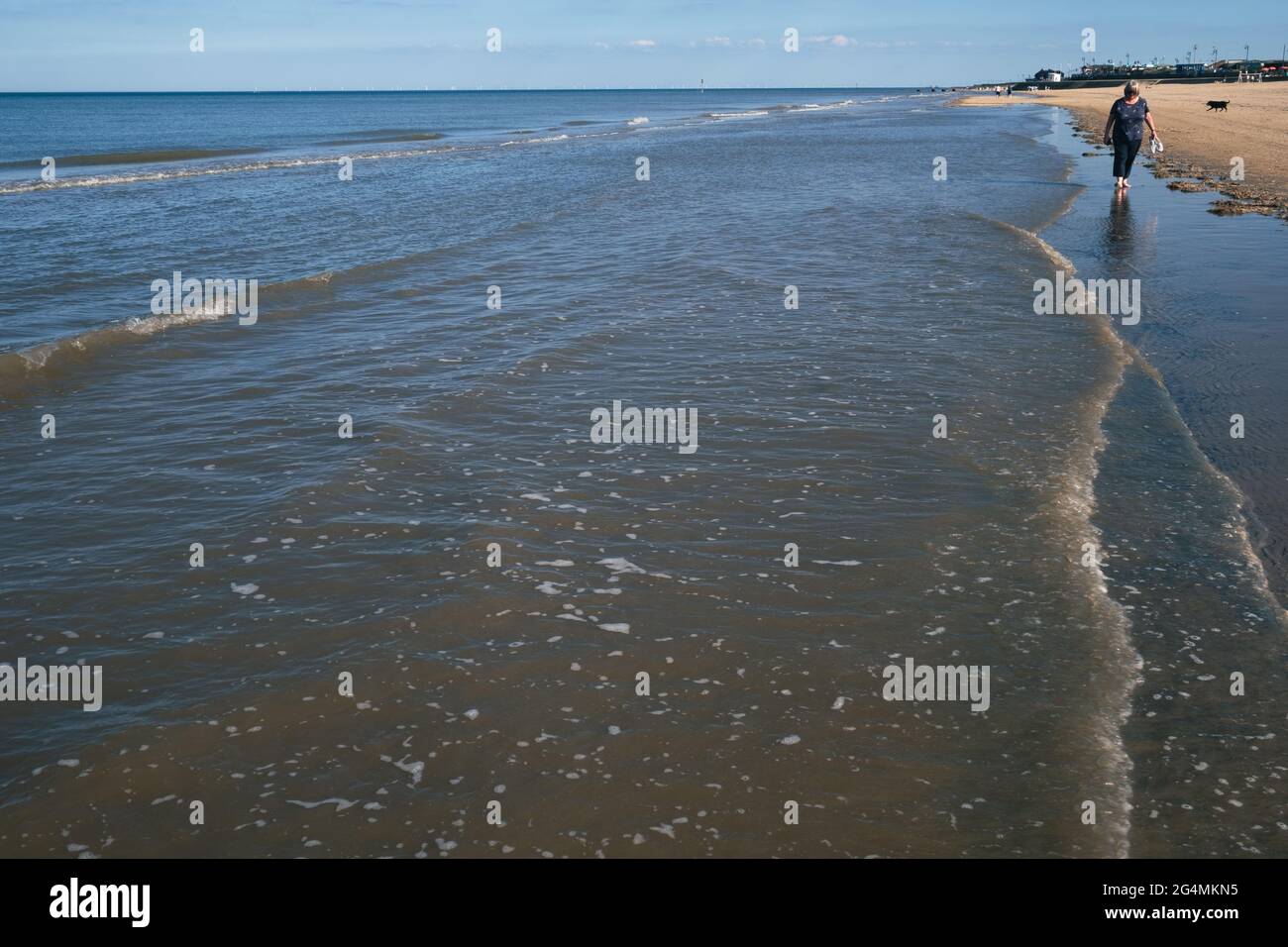 Une femme blonde d'âge moyen s'est promenée dans la mer le long de la rive nord de la plage de Mablethorpe dans le Lincolnshire Banque D'Images