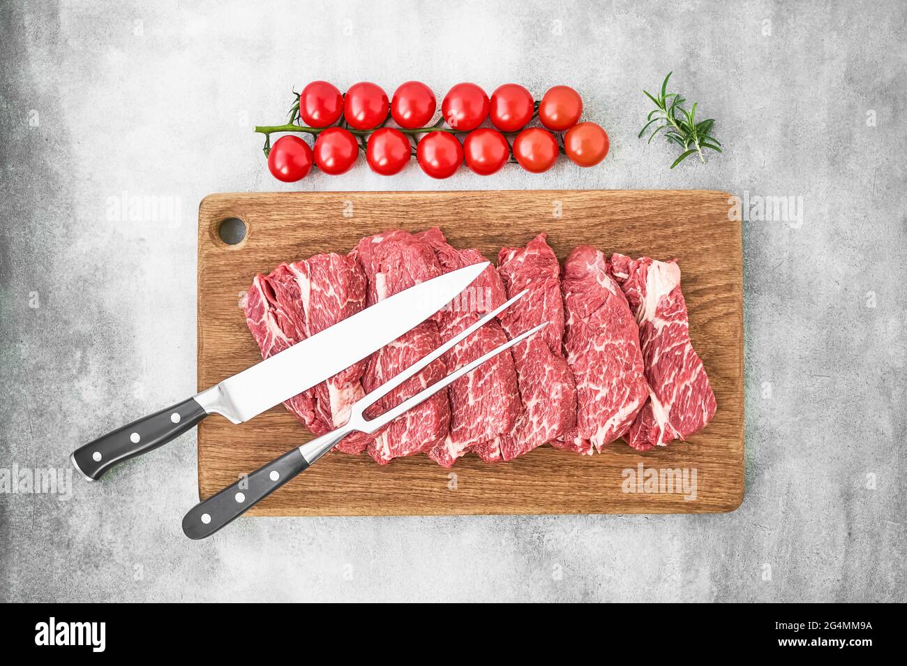 Steaks de bœuf crus au poivre et aux tomates sur planche à découper en bois sur fond gris. Espace de copie, vue de dessus. Banque D'Images