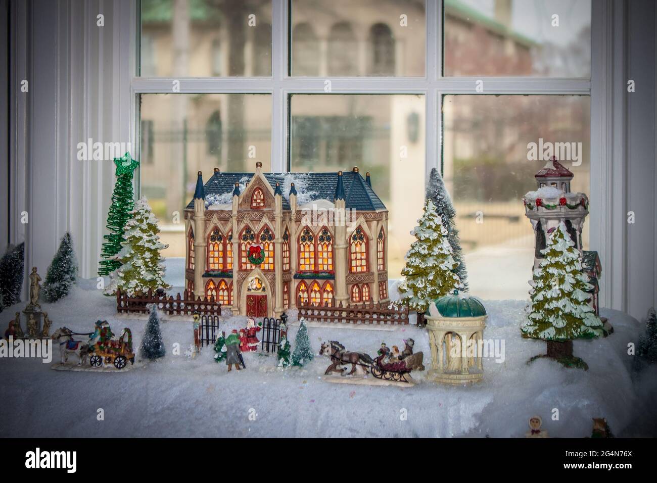Scène de village de Noël avec beau bâtiment et le père noël à la porte et les chevaux et les voitures tous dans la baie fenêtre avec manoir flou montrant à travers Banque D'Images