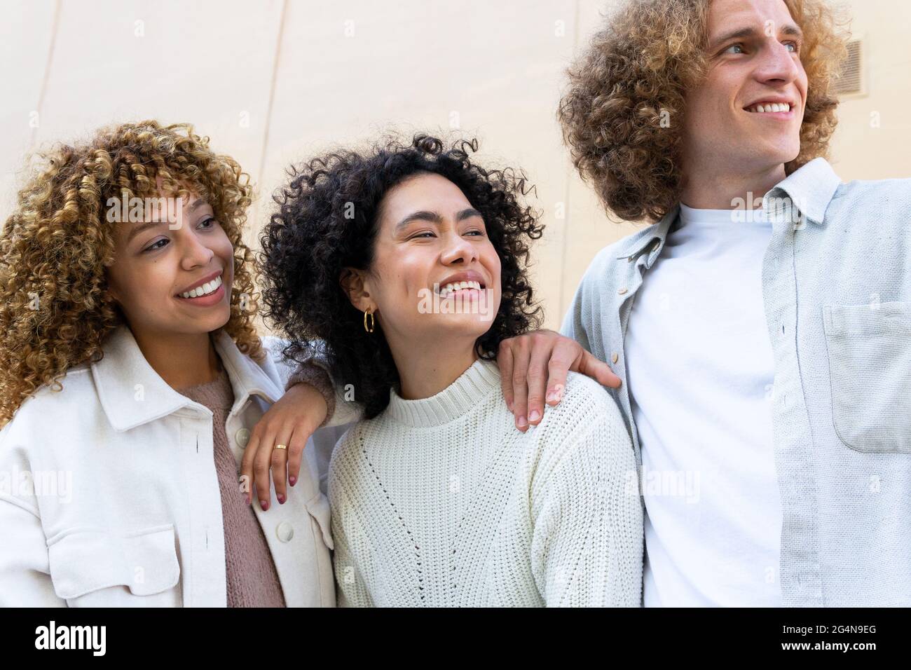 Divers hommes et femmes avec des cheveux bouclés debout regardant loin rire sur fond beige Banque D'Images