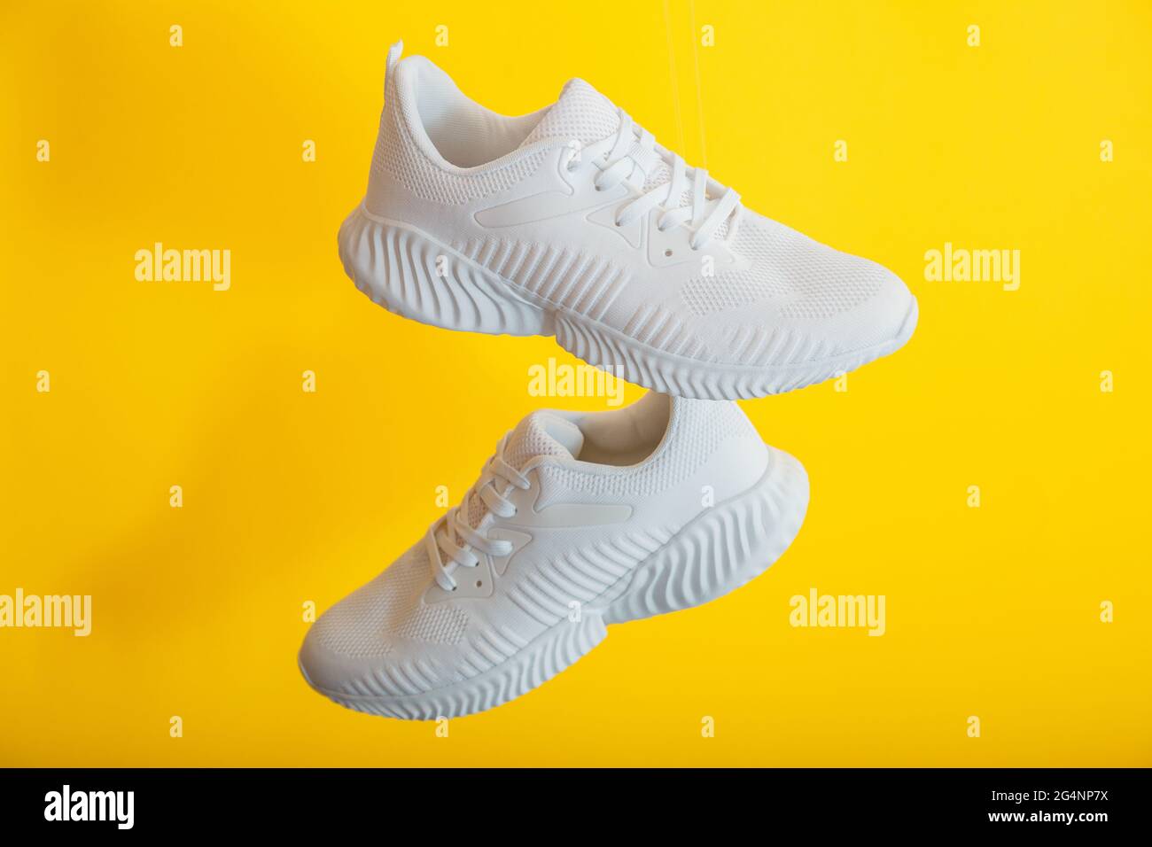 Les chaussures blanches survolent sur fond jaune. Baskets de sport pour homme. Chaussures de lévitation sur un mur jaune Banque D'Images