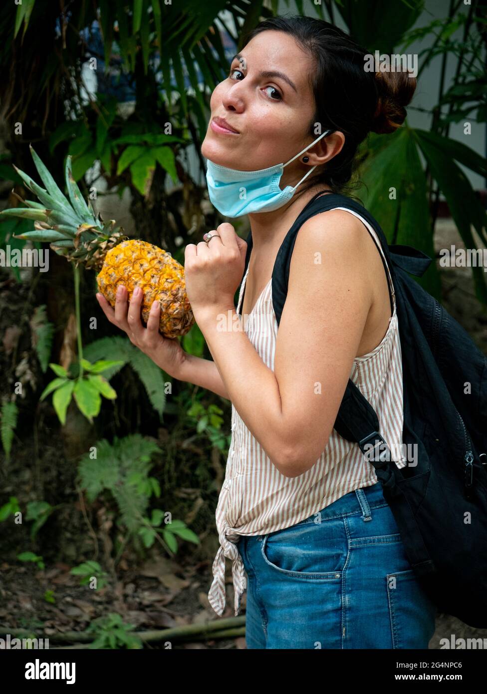 Une femme latine avec un masque sous sa bouche regarde l'appareil photo  avec un ananas dans sa main droite Photo Stock - Alamy